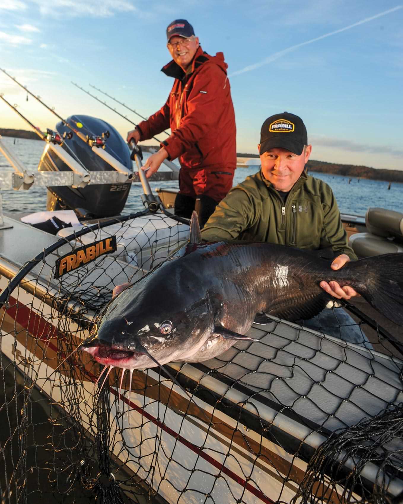 two fishers pull a large catfish catch onto their pontoon with a net