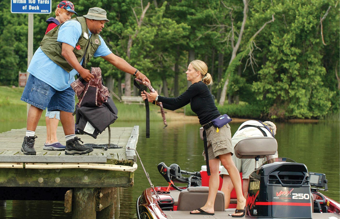 a man stands on a dock handing items to a woman on a boat